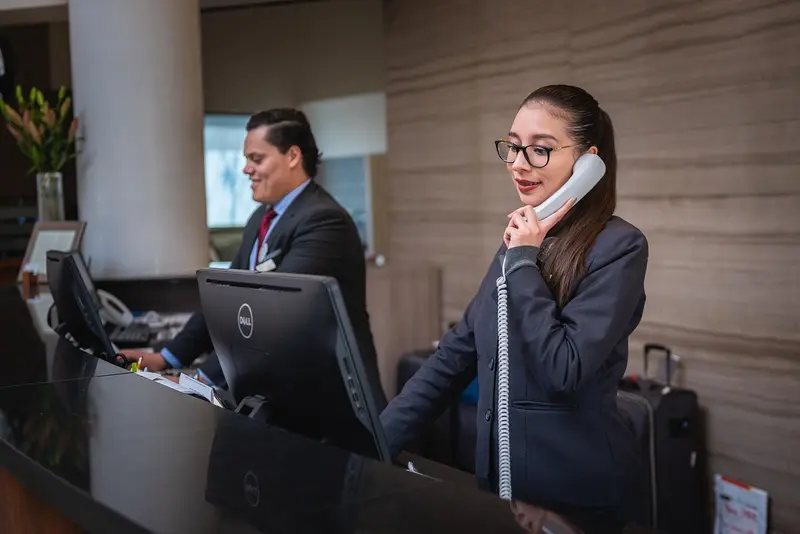 Two receptionists at a hotel are answering the phone and assisting customers, representing Dallas hotels.